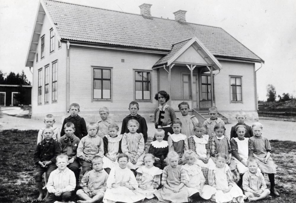Lärarinnan  Löfgren  tillsammans med skolbarnen utanför  Salby skola  vid  Västanberga gård  i  Ekskogen.  Nedre raden fr v:  Sven Jansson, Nils Davidsson,  Karin Balck, Märta Wiman, okänd,  Zackarina Sahlström, Karin Bergström  och  ? Wingqvist.  Rad 2 fr v:  Erik Gustavsson Salberga,  Arnold 'Nolle' Kraft , ? Davidsson, Karin Jansson  Västanberga, Helga Eriksson Smedby, okänd,  Linnea Jansson Ledinge,  Lilly Kraft, Svea Karlsson, Tina Karlsson  och okänd. Rad 3 fr v:  Erik Sundqvist, Sven Jansson Nibble, okänd okänd,  Anna Lönn, Kalle Karlsson  och okänd