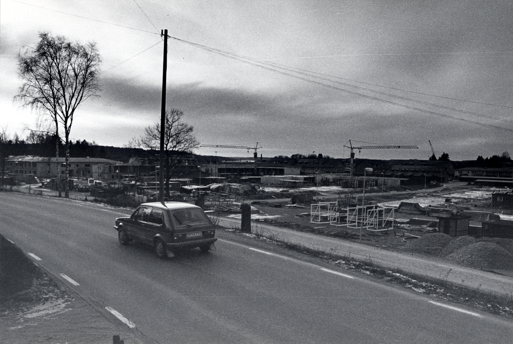 Bostadshus på  Åby gärde  byggs. I förgrunden  Lindholmsvägen  med en  Volkswagen Golf   Långt i bakgrunden skymtar Vallentuna kyrka. Bilden är tagen i närheten av nedfarten till bostadsområdet, vilken delar upp sig i Takpannevägen och Murstensvägen.