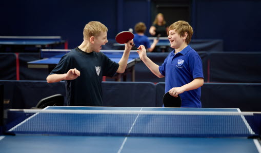 Två killar står med varsitt pingisrack vid samma sida om ett bordtennisbord.