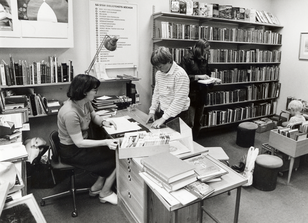 Kårsta bibliotek i stationshuset vid Kårsta järnvägsstation.  Snart skall biblioteket flytta till nya Kårstaskolan vid Bergsjövägen och bli ett integrerat skol- och folkbibliotek.  Vid disken sitter bibliotekarien Ulla-Britt Kvarnestam.  Ulla-Britt tillträdde tjänsten som filialföreståndare i Kårsta 1 november 1976