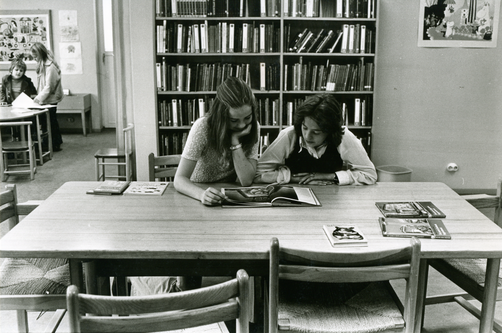 Unga besökare på biblioteket. I förgrunden sitter två flickor vid ett bord  och bläddrar i en bok.

•Fotografiet ingår i bildserien ”Vardagsliv i Vallentuna kommun” av Rachael Gough-Azmier & Gunilla Blomé, Haga Studios HB.