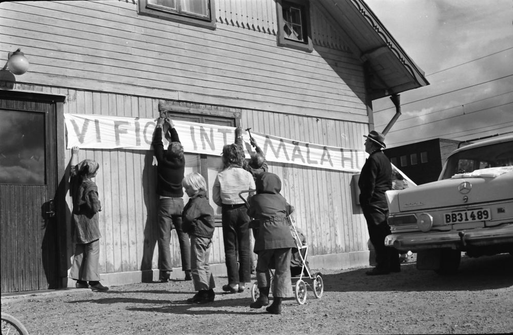 Protester mot rivning av Vallentuna stationshus. Banderoller med texten "Vi fick inte måla huset" sätts upp på stationshusets fasad. Vår framtidsmiljö, Vallentuna-Össebygruppen.

•Fotografiet ingår i bildserien ”Vardagsliv i Vallentuna kommun” av Rachael Gough-Azmier & Gunilla Blomé, Haga Studios HB.