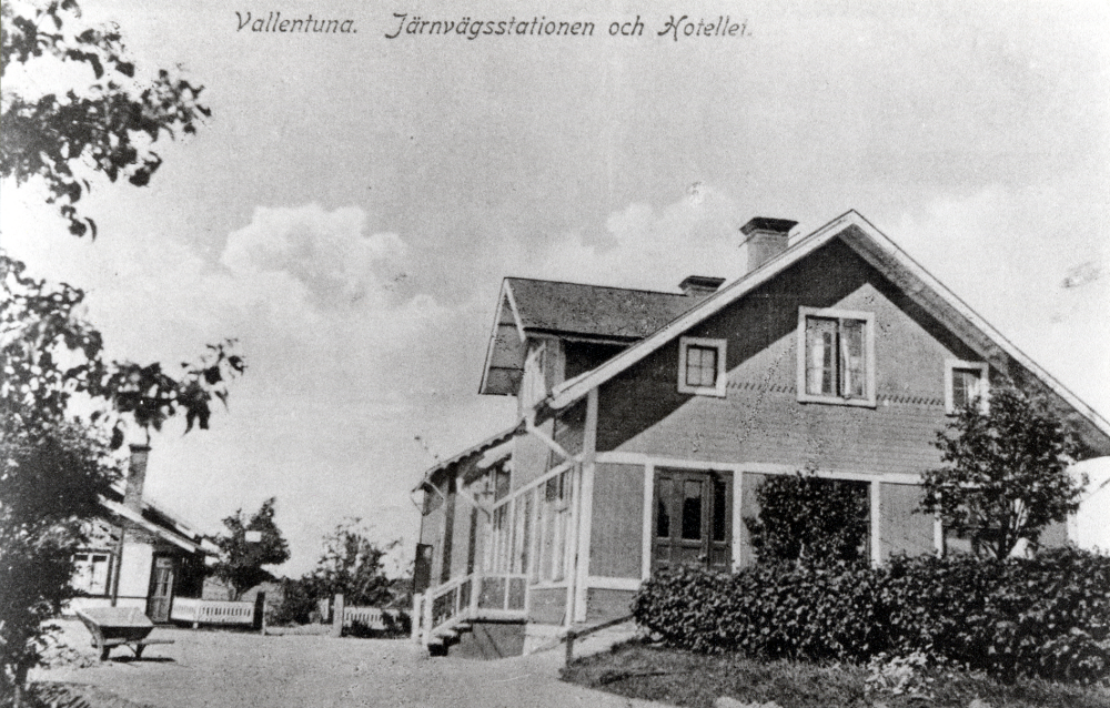 Vallentuna järnvägsstation  och  Vallentuna järnvägshotell  längst t v syns  Norbäcks bageri . På planen står en  skottkärra  Norbäcks bageri brann ner i mitten av 1920-talet.  Någon har berättat att den branden satte igång diskussioner om frivillig brandkår i Vallentuna