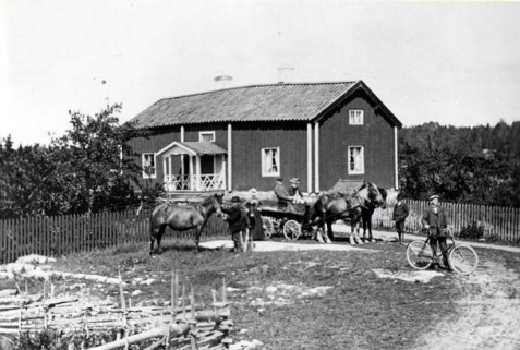 Sex personer som står framför ett hus tillsammans med ett par hästar