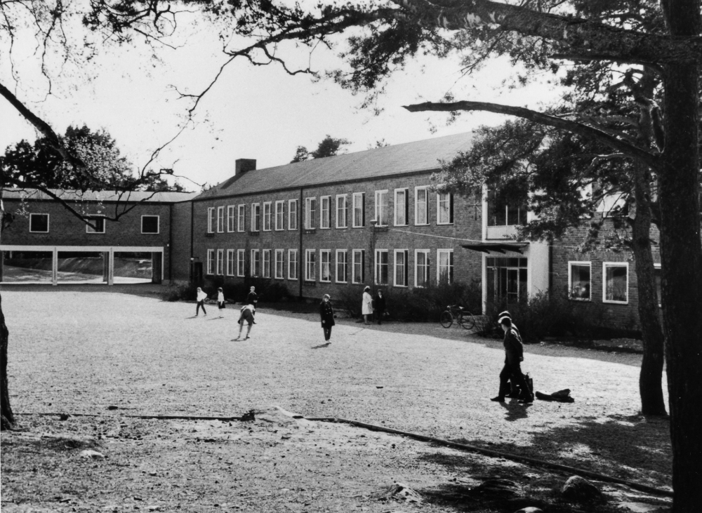 Hjälmsta skola och skolgård med den övertäckta rastgården.  Skolan byggdes som Vallentuna centralskola, men fick snart åter namnet Hjälmsta skola  och invigdes av undervisningsrådet Karnell 1954. Curt Landons arkitektkontor fick i uppdrag att göra ritningarna som påbörjades av Robert Lindholm och slutfördes av Carl Hampus Bergman. 1956 byggdes den övertäckta rastgården.  Se: Andersson, J, Från byskola till grundskola 1973.