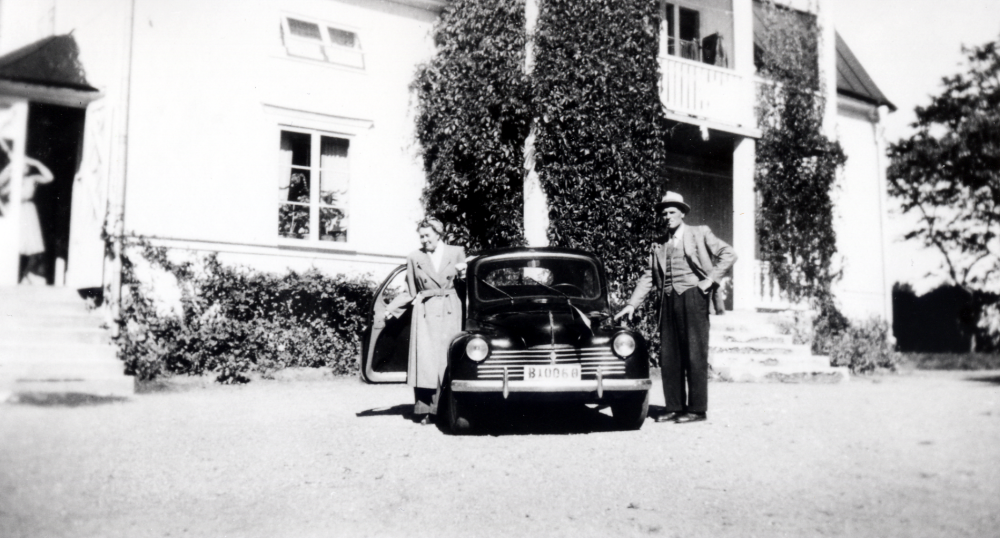 På planen utanför Ekskogens gård står familjen Ekholms första bil, en Renault  CV 4 från 1948 med registreringsnummer B 10068.  Vid bilen står gårdens ägare Manfred Ekholm t h och t v adoptivsonens Timos moster Lempi. På kökstrappan står Manfreds fru Inez