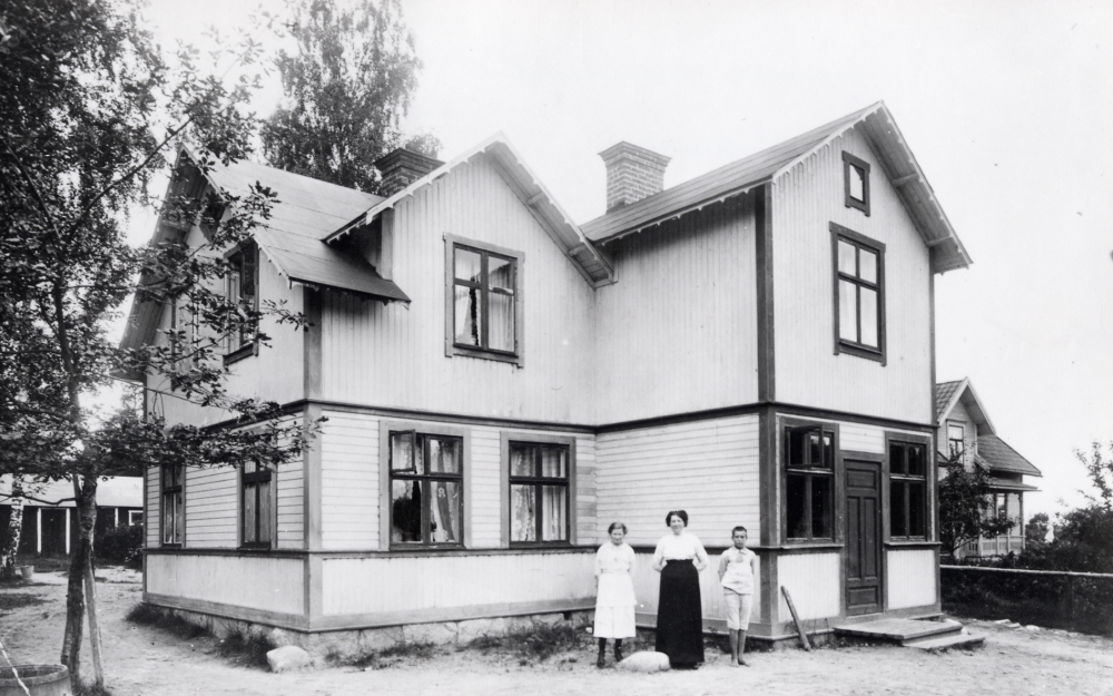 Gamla mejeriet vid Olsborgsvägen. Omkring 1915 byggdes mejeriet om, samtidigt byggdes garage, vedbod och toalett, den låga byggnaden bakom huset. Fr v mejerska Märta Johansson som var behjälplig med allhanda göromål, Maria Lindqvist som startade mejeriet och hennes son Sten Stennemark