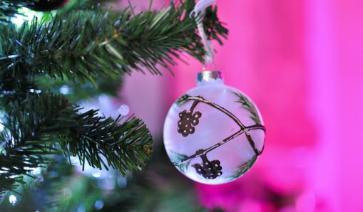 Vit julkula med dekoration  som hänger i en gran, rosa bakgrund. 
