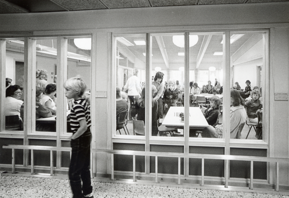 Nya Kårstaskolan vid Bergsjövägen första skoldagen höstterminen 1982 .  Skolbarnen med föräldrar och skolans personal har samlats i matsalen. En ensam pojke går i korridoren