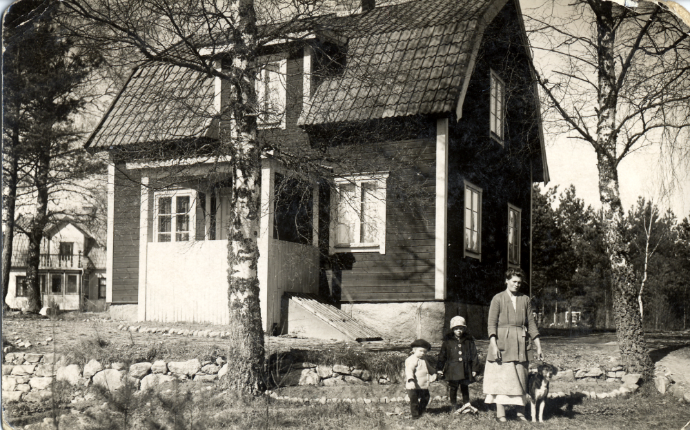 Sigridslund i Ormsta, bostad för Anna och Carl-Johan Pettersson "Brännar-Pelle".  Här står dottern Svea utanför huset med sina döttrar Gun(vor) och Harriet, båda uppväxta hos sin morfar och mormor.  Hunden heter Telle.  I bakgrunden syns Björkbacka, bostad för hönseriägaren Valle Eriksson och hans hustru Karin.  Förmodligen syns hönseriets byggnader t h om Sigridslund