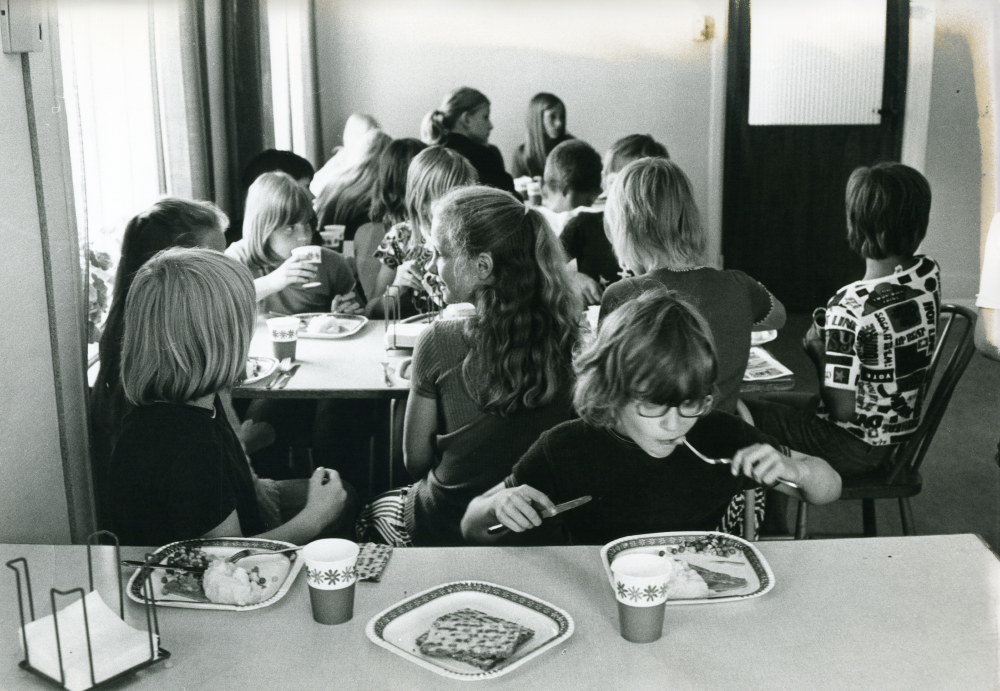 Össeby-Garns skola, dokumenterad en av de sista dagarna innan skolverksamheten läggs ner. Eleverna äter skollunch som serveras i f.d Össeby kommuns kommunalkontor. 
•Fotografiet ingår i bildserien ”Vardagsliv i Vallentuna kommun” av Rachael Gough-Azmier & Gunilla Blomé, Haga Studios HB.