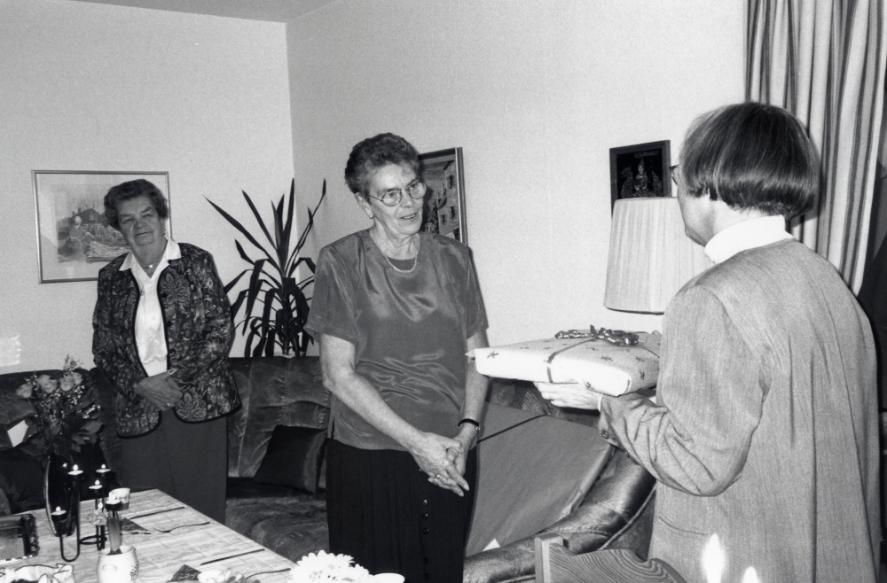Eivor Tillborg fyller 60 år och uppvaktas av arbetskamraterna på Vallentuna bibliotek.  Lena Wallén överlämnar den gemnsamma presenten - en linneduk.  I bakgrunden står Eivors  mamma Karin Ritzén