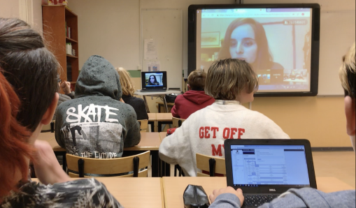 tonåringar sitter framåtvända mot en digital skärm i ett klassrum.