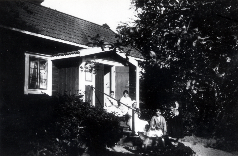 Mörbydal. Överst på trappan fr v okänd, Julia Gustafsson, på trappsteget nedanför sitter Hilda Lindberg med en liten valp i famnen. Mannen är Gottfrid Lindberg. De små barnen i en skottkärra? är fr v okänd, Iris Lindberg och ev Allan Gustavsson. Damen längst t h med en valp i famnen är Ester Jansson