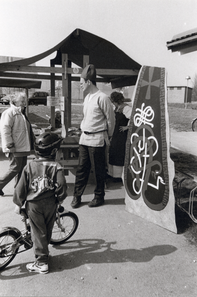 Karby torg invigs.  Karby bibliotek i samverkan med ICA Brottbyhallen och post i butik – allt under samma tak.  Runt torget i stånd presenterar olika föreningar sin verksamhet.  Här visar Össeby hembygdsförening runsten och bokbord.  Föreningens ordförande Börje Sjöman är klädd i "vikingakläder".