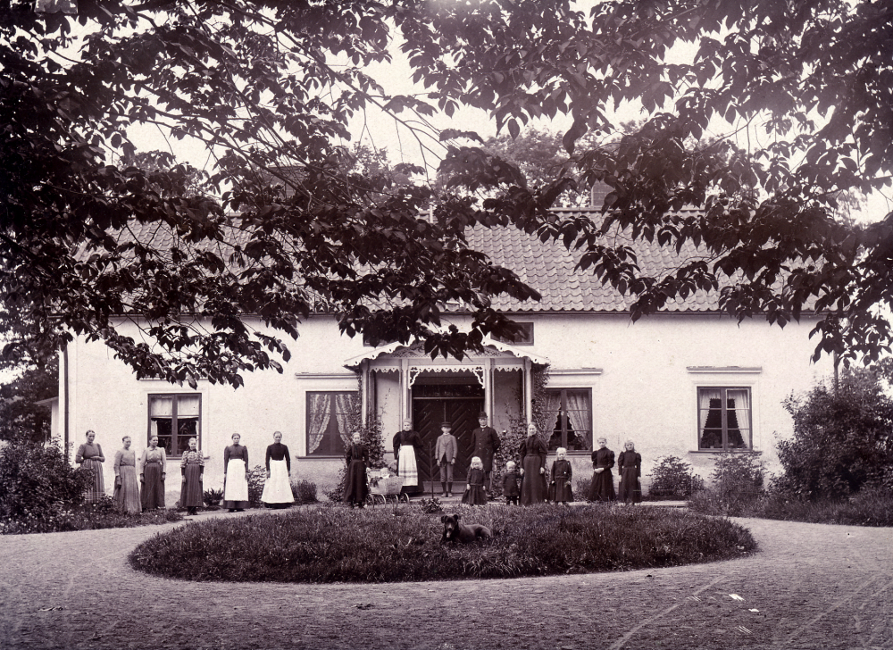 Frösunda prästgård revs 1917. En ny byggnad uppfördes på samma plats.  

C G Sandahl var kyrkoherde i Frösunda 1885-1898/1900 då han flyttade till Norrtälje. Ev kan personerna på bilden tillhöra hans hushåll med familjen i centrum och tjänstefolket t v.  Fotograf ev Zackeus Carlsson