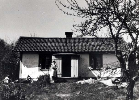 Hus. Framför huset står en kvinna.