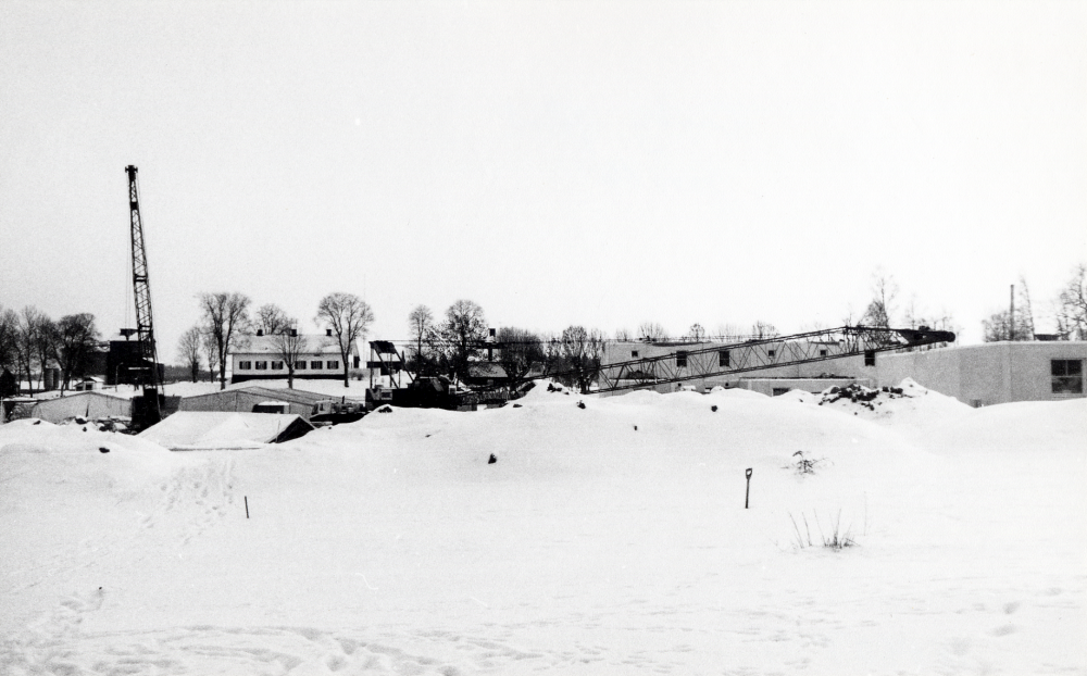 I bakgrunden Stora Karby gård. I förgrunden framför hyreshusen med adress Tallstigen byggs ett nytt bostadsområde med bostadsrättshus i olika storlekar.  Området får adress Lindgårdsvägen