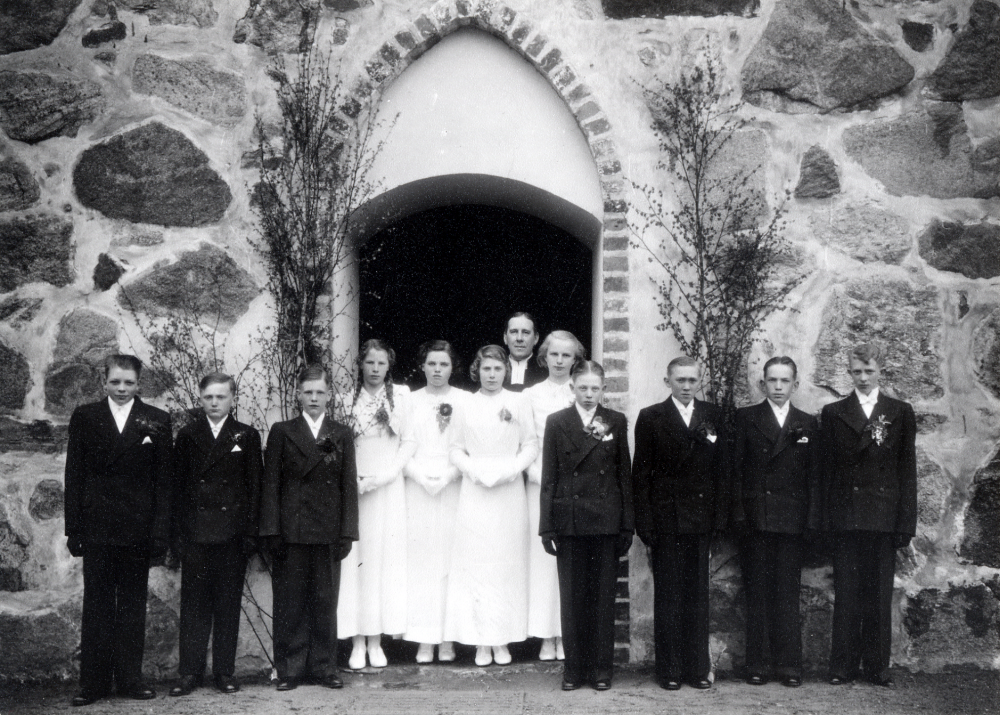 Konfirmation i Frösunda kyrka. Bakom konfirmanderna står kyrkoherde Paul Sjöberg. Fr v Rune Nyberg, Martin Grandin, Sven Andersson, Karin Lundkvist, gift Wahlström,  Elvy Jansson, Gullan Wadström, Stina Andersson  gift Thorsaeus, Sixten Helgöstam. Rune Jansson från Rolsta, Berthold Östervall och Edgar Axzell  Uppgifter: Rut Ekstedt och Stina Thorsaeus