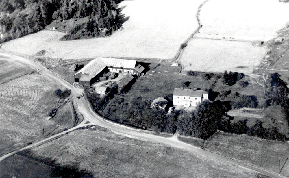Flygfoto över Väsby gård i Vallentuna.  Sven-Erik Karlsson arrenderade gårdens marken från 1963 till 2003.  Gården revs 1971 när bostadsområdet Sörgården byggdes.  I bakgrunden på fältet syns gårdens ungdjur beta.  I bildens mitt t  h syns tvättstuga och smedja.  I trädgården t h om huvudbyggnaden fanns ett sextiotal äppelträd.  Fröknarna Carlsson (Sven-Eriks gammelfastrar)som tidigare ägde gården, odlade där äpplen som de sålde till Stockholm.  Bilen som står på vägen är Sven-Eriks Chevrolet lastbil.  Gamla vägen mot Upplands Väsby går förbi gården