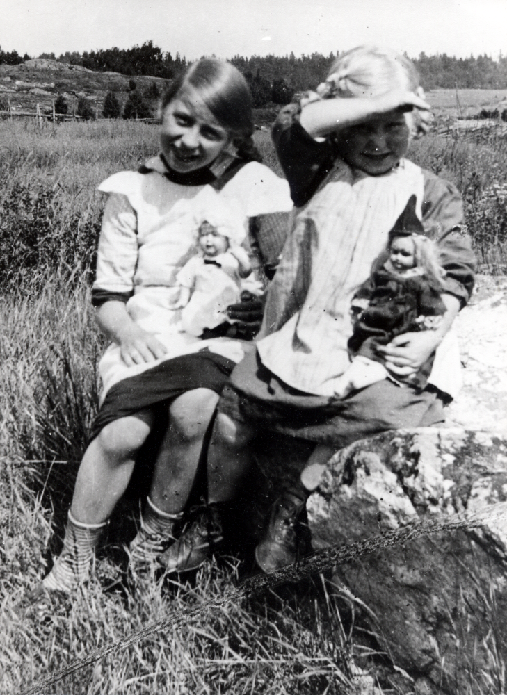 Sara Schenström hälsar på hos mormor Charlotta Pettersson i Lilla Mörby, Orkesta.  Sara är född 1903 och lever fortfarande 2005. Charlotta arrenderade tidigare Stora Mörby tillsammans med maken John.  Efter hans död flyttade hon till undantagsstugan i Lilla Mörby.  Hennes dotter Gerda hade tillsammans med maken Conn Schenström barnen Ragnar och Sara.  Här leker Sara tillsammans med Charlottas fosterdotter med sina dockor vid stugan