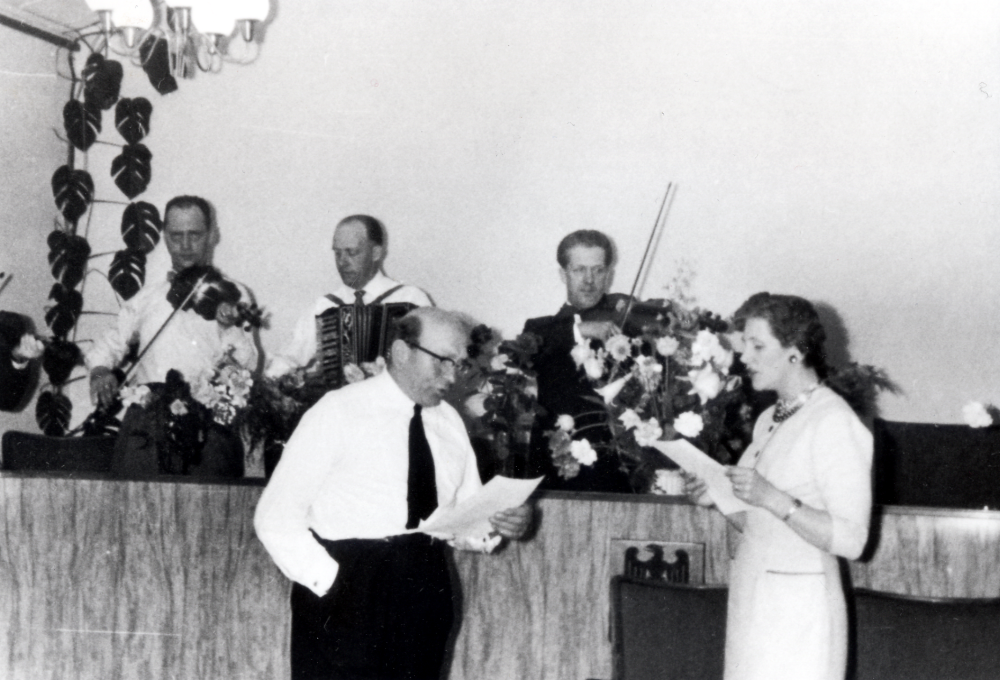 Hans Uhrenius fyller 50 år i maj 1957 och har fest i Kommunalhusets sessionssal.  På podiet sitter en tremannaorkester, längst t v kommunalingenjören Petter Nordin med fiol.  T v framför podiet står Gustav Nilsson, kommunalnämndens ordförande 1952-1955, samt  Lennart Uhrenius sambo