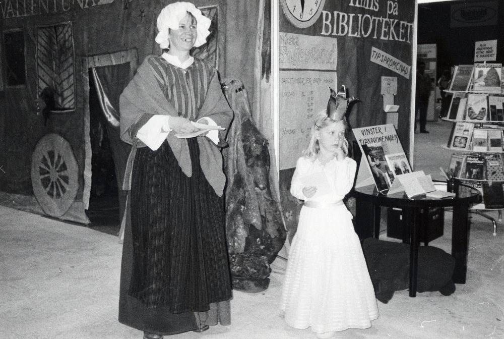 Vid Föreningarnas festival i Vallentuna ishall 19-21 april 1986 fick föreningar och kommun presentera sin verksamhet med utställningar, sång och musik. Här syns Vallentuna biblioteks monter byggd som en bokbuss med sagogrotta. Utanför står Lena Lundgren beredd att läsa sagor. Bredvid henne prinsessan Sara Ullman