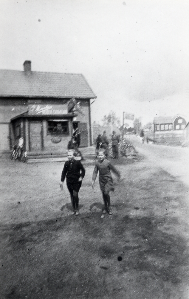 Riksmarschen vid kiosken i Angarn.  De två flickorna är t v Lilly Wass gift Öhlin och Gerd Johansson gift Bergkvist t h.  I bakgrunden t h syns Angarns småskola.  Marschen ägde rum 1941 och var ett säreget arrangemang för att höja medborgarandan.  Män marscherade 15 och kvinnorna 10 km inom en bestämd tid.  Poängen räknades i relation till Sveriges och Finlands folkmängd. Många deltog i traditionell Sverige-Finland friidrottsanda.  Finlands president och statsminister deltog under stor mediebevakning. Sammanlagt deltog 1 507 111 finländare  och vann över Sverige i detta evenemang som var säreget i hela världen.  Man hade lyckats stärka gemenskapsandan.