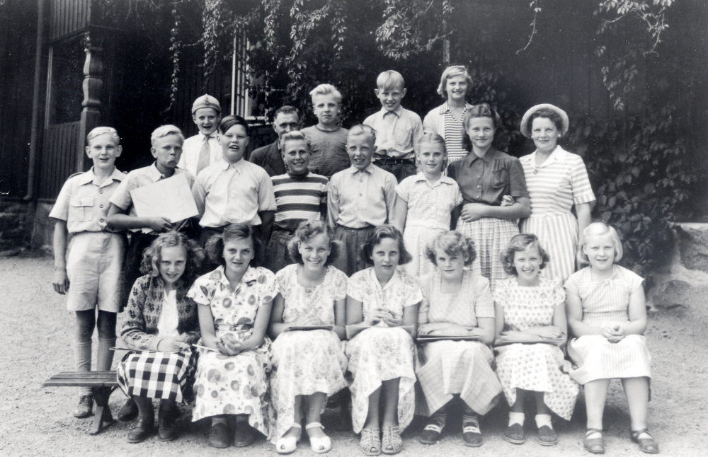Lärarinnan Edit Lindström md elever utanför Röda skolan under en teckningstimmer, barnen har papper i handen. Övre raden fr v Bror Lundkvist Brollan, vaktmästare Karl Nilsson, Uno Hoff, Bo Olsson och Birgit Jansson. Mittenraden fr v Hans-Erik Åkerström Luva, Bengt Berg, Hans Nordström Nappe, Erik Åman, Mona Lutteman, Märta Fällman och lärarinnan Edit Lindström. Sittande fr v nr Ingrid Nilsson, Ingegerd Hedlund Fimpens lillsyrra, Gerd Johansson, Maud Wängelin Wängelin, Solveig Eriksson (fosterdotter hos Gösta Karlssons åkeri), Mona Skogsberg ochElsy Andersson