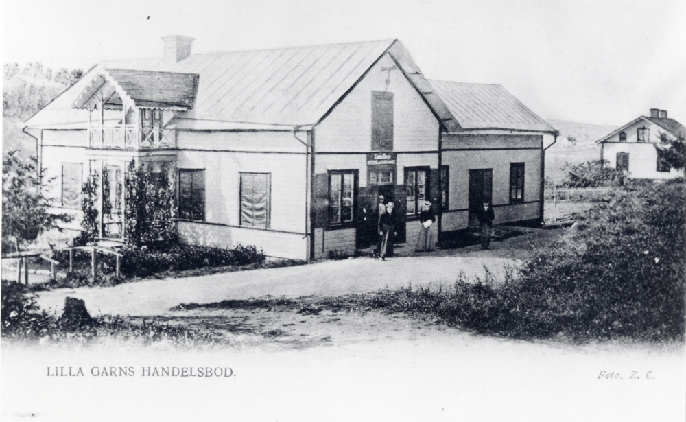 Lilla Garns Handel i Garns Kyrkby. Byggdes 1909 på en plats där en annan byggnad delvis stått och då vid den på bilden större vinkeldelen mot Klockaregården längs Garns-Bergavägen. Fastigheten ägdes och byggdes av Isidor Bergs Speceri- och Diversehandel. Isidor Berg bodde i Gustavsberg, Kårsta och bedrev handel även där samt i Närtuna. Samtliga affärer sköttes inom släkten.I Garn Kyrkby av hans Fru, under namnet "Ebba Bergs Lanthandel" Senare under 1940-talet byttes ägare till C.J. Erikssons Diversehandel och än senare bröderna Lindell. Slutligen togs rörelsen över av ena brodern Martin Lidell som drev handeln till 1964, då affären upphörde och gjordes om till bostad. Vinkeldelen var då sedan länge riven. På andra sidan om vägen finns än i dag kallkällaren kvar som användes för kylda drycker, salt sill m.m.
Efter nedläggningen av affären ersattes den av matbussar,
en privat och en från Konsum. Den privatägda lade ned verksamheten 1971 och Konsum 1972.
Det vita huset t h är Klockargården, numera rödmålad.
Uppgifter John-Lars de Chasseur. Backebo Garnsberget för Roslagsporten Kultur