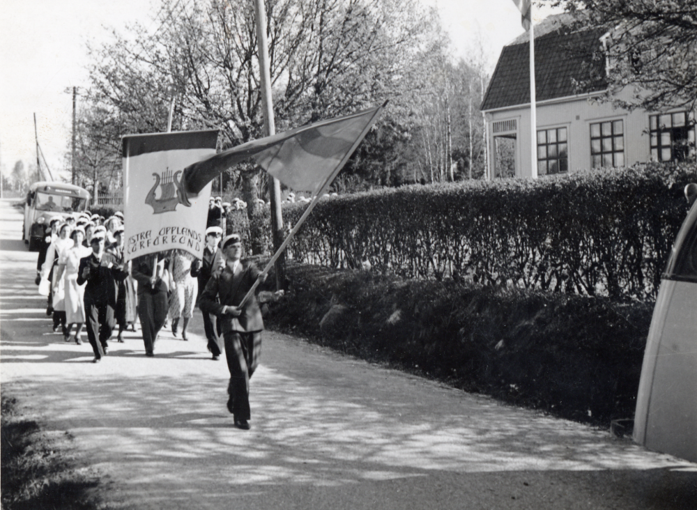 Östra Upplands körförbund  på väg nerför  Skolvägen  förbi  Hjälmstaskolan   Vita skolan  mot  Vallentuna kyrka  för att hålla konsert i kyrkan.  Fanbärare  är körens ordförande  Arne Lindström     I bakgrunden på Skolvägen syns en  SLO-buss