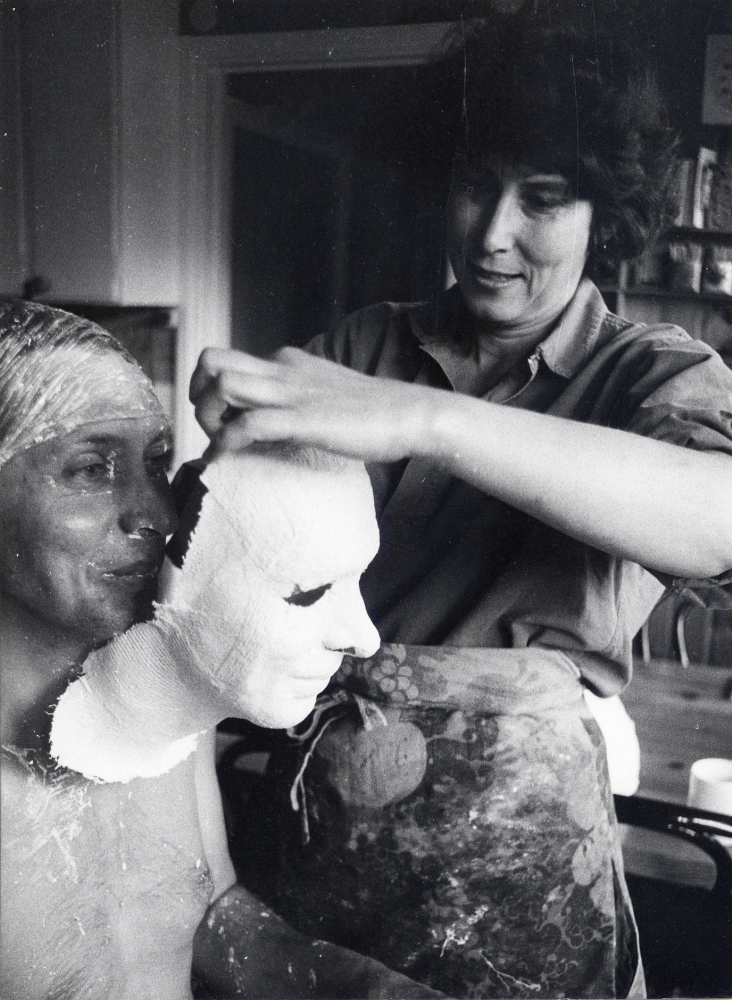 Eva Rahmqvist gjuter av ansiktet på Gunnar Hillbo med hjälp av gipsbindor. Masken skall användas till ansiktet på en snickare på Läckö slotts sommarutställning Trä 1987. Ansiktet smörjes in med vaselin och gipsbindor, klippta i små bitar och doppade i vatten, läggs på ansiktet. Efter en stund dras gipset bort och Eva modellerar sedan ett huvud med utgångspunkt från det gjutna ansiktet. Här lyfter Eva bort den halvstelnade masken från Gunnars ansikte och hals. Foto från Eva Rahmqvists hem, Bällstavägen 59 C
