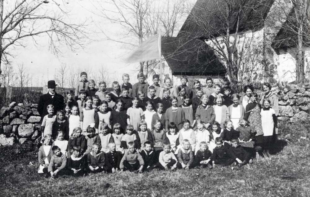 Lärare och skolbarn samlade utanför kyrkmuren vid  Össeby-Garns kyrka   Martin Lewald  längst t v, lärare för klasserna 5 och 6. Längst t h  Nanny Skoglund  klasserna 1 och 2, samt bredvid henne  Ruth Nilsson  klasserna 3 och 4.