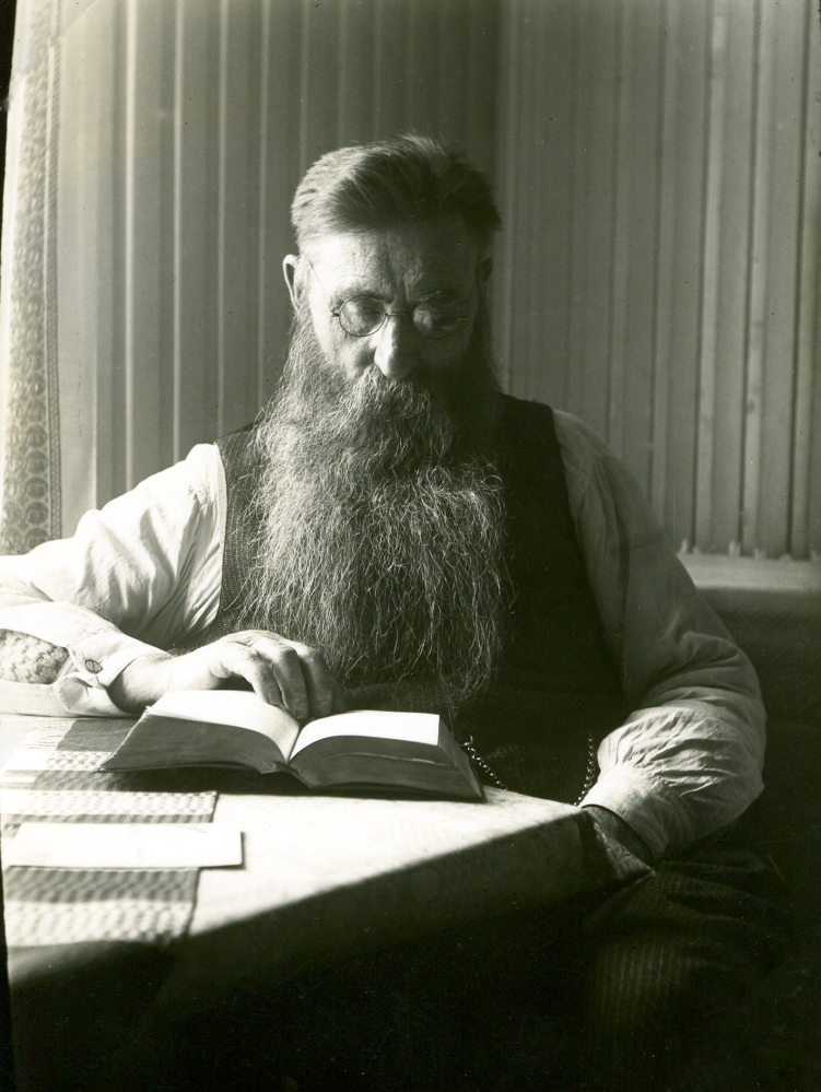 August Ländin från Kårsta sitter vid köksbordet i Backatorp och läser bibeln. Han var torpare under Backa gård och även fjärdingsman i Kårsta. August levde 1863 till 1935, var gift med Emma Augusta, som levde 1866 till 1933, de hade 11 barn tillsammans