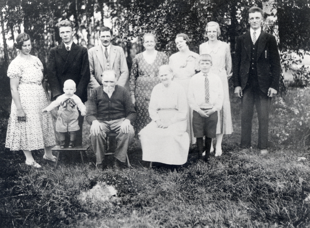 Vilhelm och Charlotta Nyberg vid Karlsro i Fasterna har fyllt 80 år och samlat barn och barnbarn till ett gruppfoto.  I  bakre raden fr v står Mia Karlsson med maken (eller blivande maken) Gunnar Nyberg, Valfrid Nyberg, Amanda Nyberg, Karin Nyberg (gift Ritzén), Lilly Nyberg (gift Eriksson) och Helge Nyberg.  Nedre raden fr v Tore Nyberg, Vilhelm Nyberg  född 22 augusti 1852 (far till 3, farfar till 2 och farfars far till 8) och Charlotta Nyberg född 24 augusti 1852 samt Rune Nyberg. Amanda och Valfrid är föräldrar till Helge, Gunnar, Karin,  Lilly och Rune.  Vilhelm och Charlotta är morfar och mormor till Stig Öhman, Åttesta i Frösunda