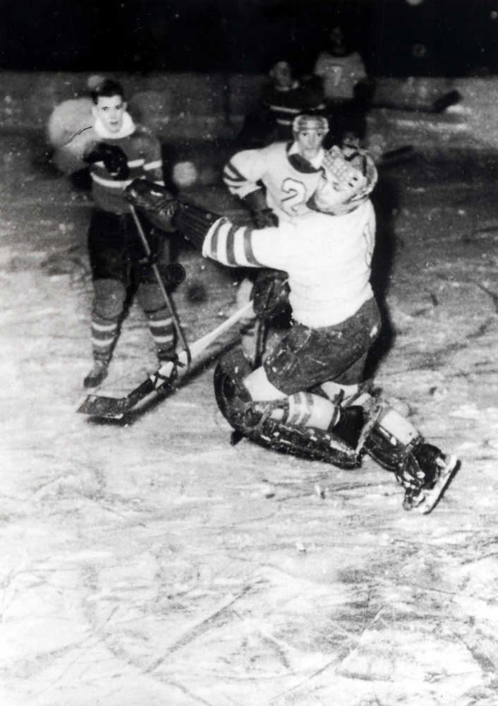 Ishockeymatch på planen vid Kärret i Karlberg under första halvan av 1950-talet.  Förmodligen en match i "Klubban-turneringen" mellan VBK och Enebyberg.  Vissa detaljer är iritade med svart på origialfotografiet, förmodligen som förstärkning vid publicering av bilden