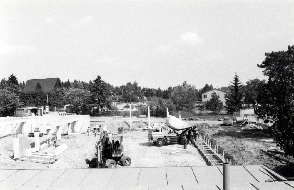Det nya Domusvaruhuset byggs i Vallentuna centrum.  De första elementen till våningsplan 1 har kommit på plats.  En grävskopa arbetar  och en betongbil tippar betong i en gjutform.  T v syns Pingstkyrkan och t h Centrum Bio