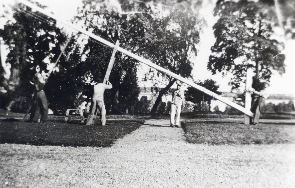 Vallbostrands vårdhem - Bällsta gård i Vallentuna.  På planen reses flaggstången.  Två man med långa "träsaxar" lyfter sången och en man står vid flaggstångsfundamentet.  Mannen i mitten kan ev vara "Verner".  I bakgrunden syns Vallentunasjön