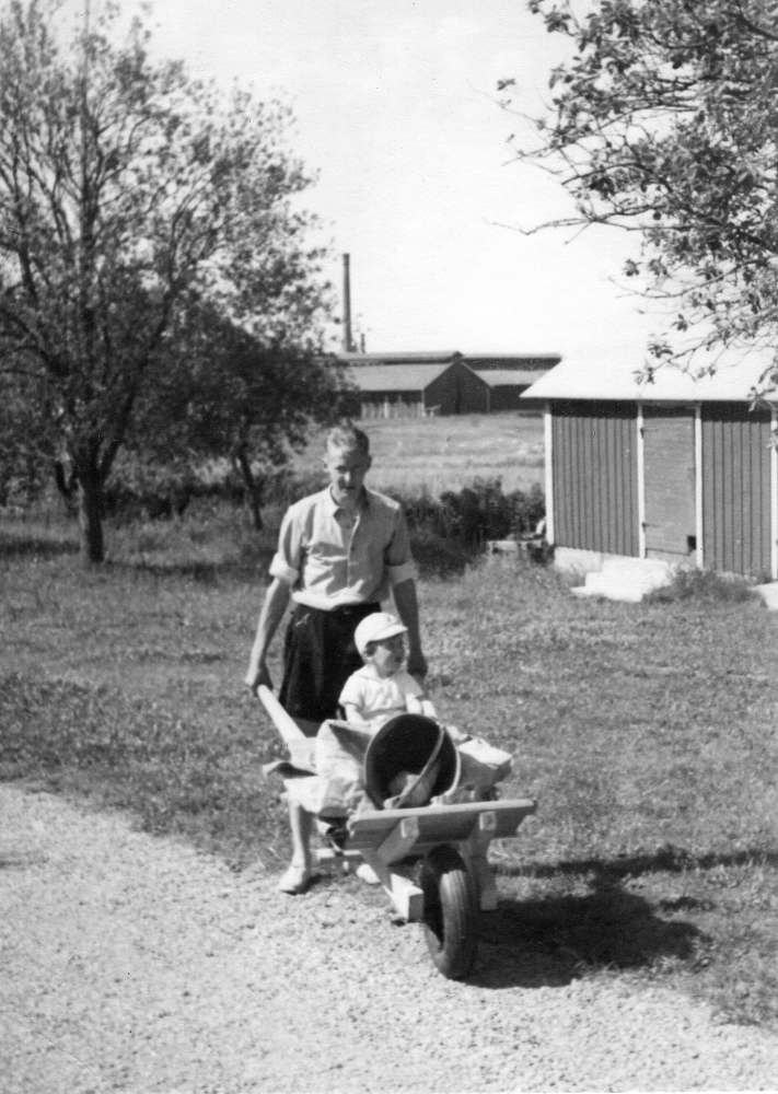Ragnar Pettersson med sonen Gunnar i skottkärran vid Bjrökhult i Vallentuna, familjens bostad fram till 1952.  Bjökrhult låg söder om nuvarande Ormstavägens utfart mot Lindholmsvägen.  I bakgruandens syns Åby tegelbruks byggnader
