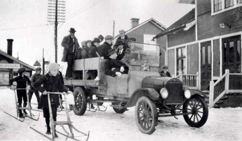 Bandylaget  i  Vallentuna bollklubb VBK  rycker ut för bortamatch i Sigtuna. Pojkar med  sparkstöttingar  ser på avfärden från  Vallentuna järnvägsstation.   Lastbilen  på vars flak bandylaget står, tillhörde Ingvald  Gustavsson eller hans bror.  I bakgrunden t v syns  Norbäcks bageri  som brann ner 1924