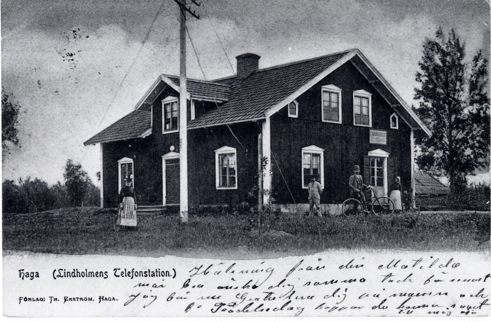 Haga växelstation  i  Lindholmen. Framför huset står en man med  cykel. Ytterligare en man samt två kvinnor med  förkläden står vid huset. Bakom huset vid höger gavel syns ett  halmtak.  Från gaveln fanns ingång till Hammarstedts affär