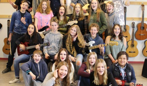 barn i mellanstadieåldern sitter glada tillsammans och håller upp olika sorters instrument, mestadels gitarrer.