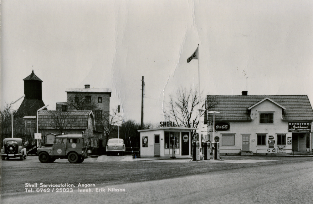 Begsättra i Angarn med café och Shell bensinstation. När bilden togs var Erik Nilsson innehavare (text på fotot). Här har också Seth Abel Axén (1899-1986) drivit café och bensinstation tillsammans med hustrun Ruth (1904-2003) samt systern Olga Axén (död 1951). Seth började med en kiosk på 1930-talet. 1947 byggdes fastigheten om. Kopia av ett vykort.