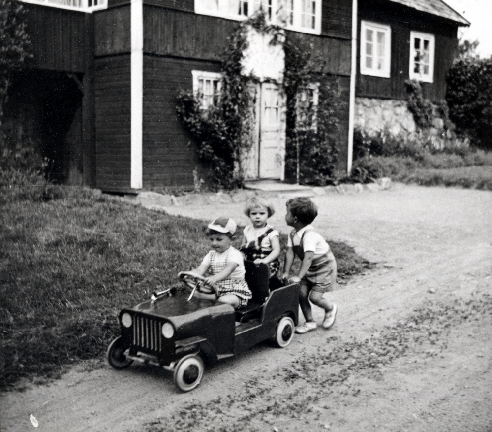 Håkan och Britten Helgöstam samt Per Linder kör trampbil som ser ut som en jeep utanför gamla Helgö gård.