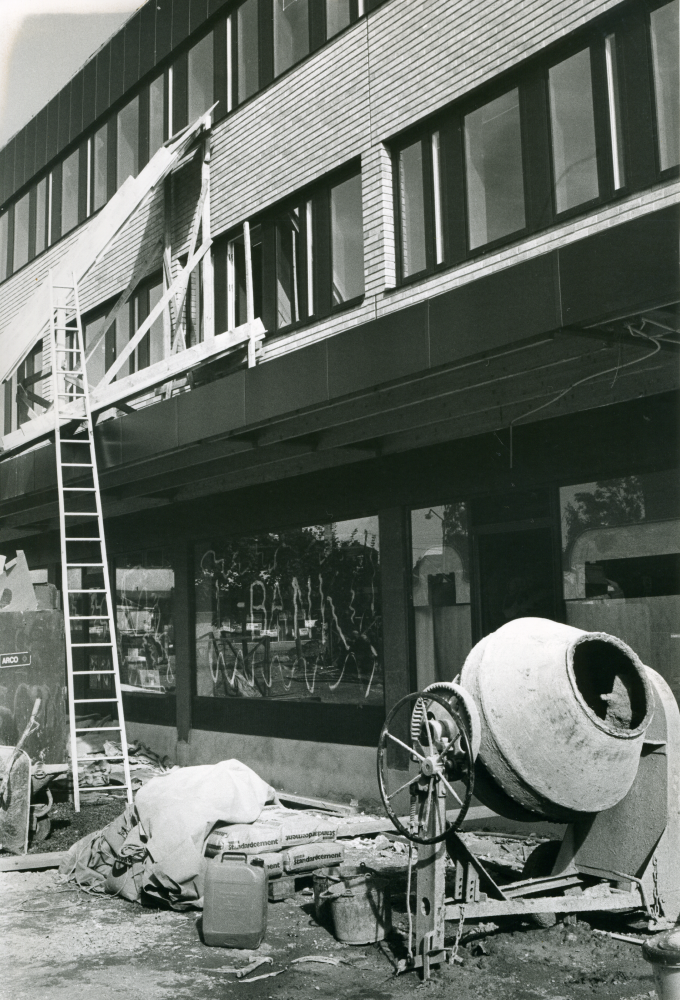 Butiker och hyresgäster ska snart flytta in i det nybyggda Tunahuset vid Tuna torg. Här pågår fortfarande byggarbetet. På torget står en cementblandare och en stege är rest mot fasaden.
•Fotografiet ingår i bildserien ”Vardagsliv i Vallentuna kommun” av Rachael Gough-Azmier & Gunilla Blomé, Haga Studios HB.