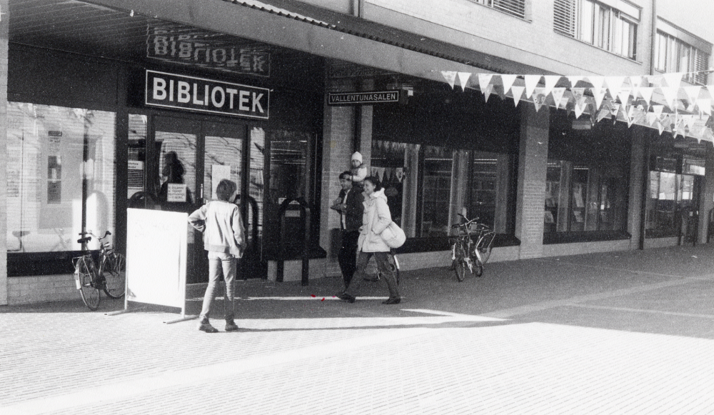 Entrén till Vallentuna bibliotek som firar Frimärkets dag med flaggspel mellan Tärningen och Domus. På väg in i biblioteket fr v Magnus Hillbo och t h Curt Brathén och Margareta Brathén med sonen Fredrik Brathén