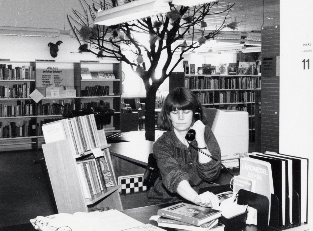 Låneexpeditionen i Vallentuna bibliotek . Bakom disken sitter Lena Lundgren och talar i telefonen