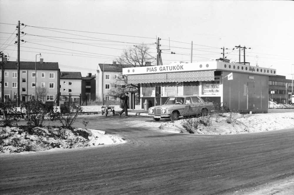 Pias gatukök vid Vallentuna station. I bakgrunden till vänster syns flerfamiljshusen vid Centralvägen, till höger skymtar Tunahuset.
•Fotografiet ingår i bildserien ”Vardagsliv i Vallentuna kommun” av Rachael Gough-Azmier & Gunilla Blomé, Haga Studios HB.