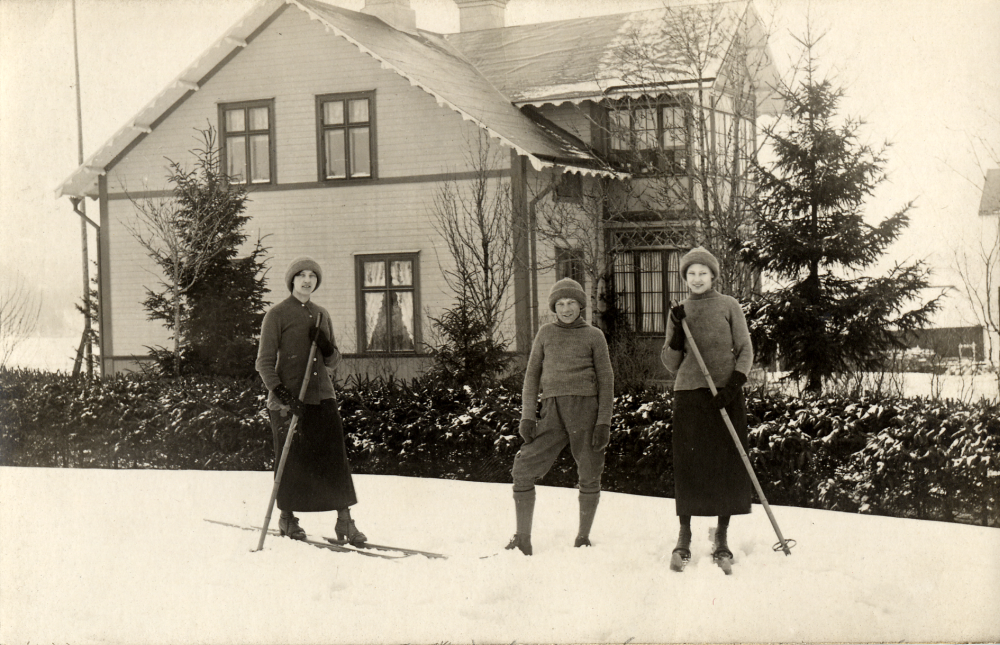 Henriksborg i Kårsta med tre ungdomar Sundqvist?  Båda flickorna har skidor med en stav.  Vykort med texten: Kårsta den 10/5 1915.  Kära Anna!  Som jag var i Sthlm förra veckan, så gick jag upp till dig för att helsa på, men sorgligt nog var du ej hemma (jag skulle ju ha telefonerat först förstås) derför skickar jag dig nu ett litet kort af vår villa jemte en "del af mitt menageri".  Den äldsta av dem förlovade sig häromdagen vilket du kanske såg i tidningen.  Wi få väl försöka att träffas en annan gång.  De hj helsningar från din gamla ???? Hilda S