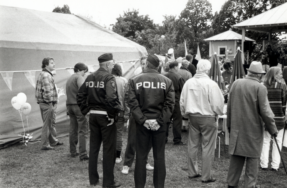 Svenska nationaldagen firas i Vallentuna.  Festligheterna inleds med tal i kommunalhusparken övervakade av polisen.  Mannen med käpp t h är Gustav Nilsson